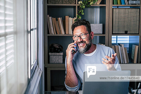 Male freelance worker gesturing while talking on smart phone at home office