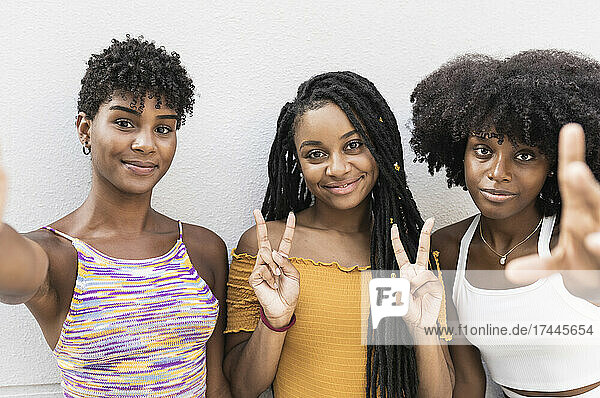Young women gesturing peace sign in front of wall