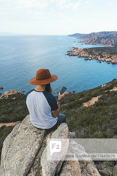 Mann mit Hut benutzt Smartphone auf Felsen