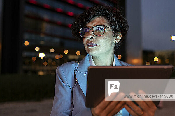 Beautiful mature businesswoman wearing eyeglasses holding digital tablet at night