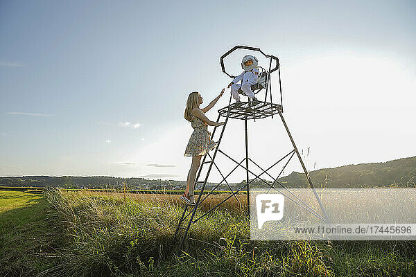 Mother reaching to son sitting on lookout tower at field