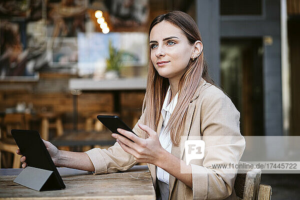 Businesswoman with mobile phone and digital tablet sitting at coffee shop