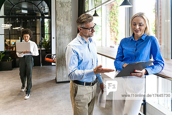 Business professionals discussing over clipboard in office