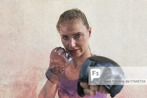 Female boxer showing punching gesture in front of wall