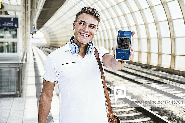 Happy man showing vaccination qr code on smart phone screen at subway platform