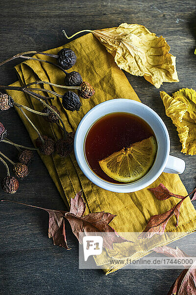 Cup of tea with lemon and dry leaves on wooden table