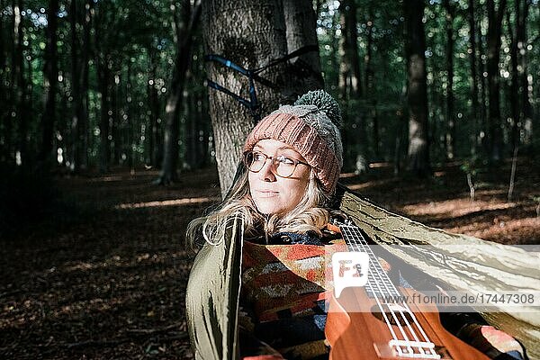woman sat on a hammock in a forest with a ukulele in autumn