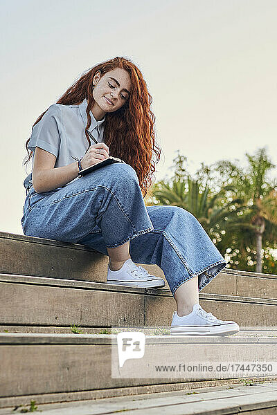 Young redhead woman writes in a notebook outdoors