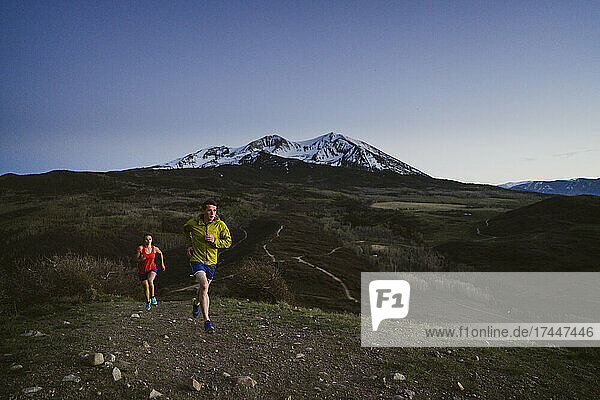 A man and woman trail run at dawn with mountains in the distance