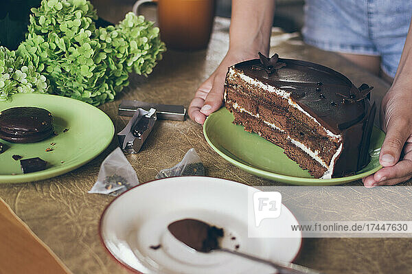 Hands put plate with chocolate cake on table