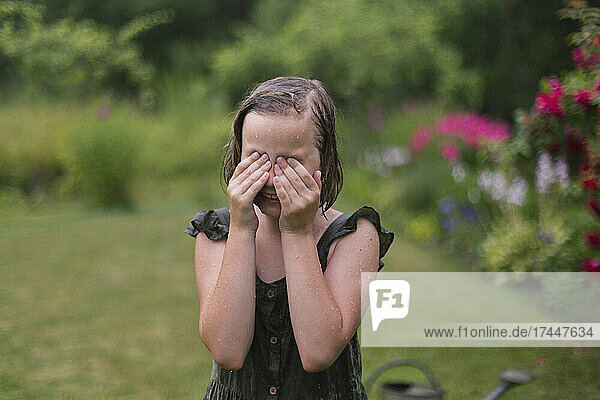 Girl in the rain wipes her eyes in her garden.
