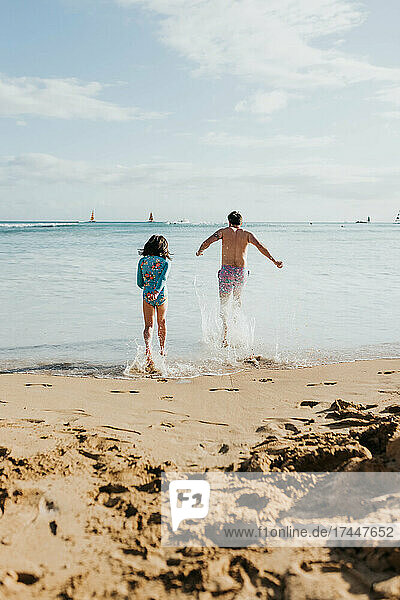 Father and daughter run and play in ocean on beach in Waikiki