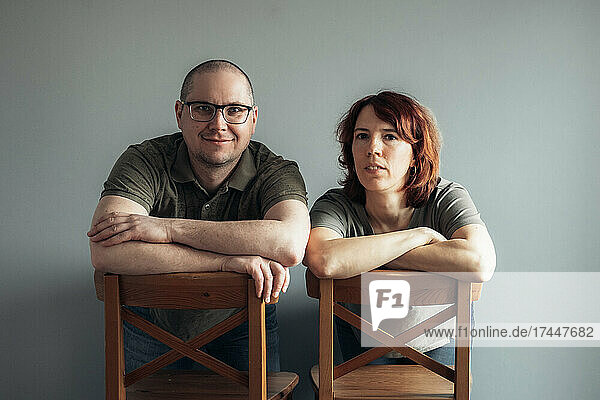 Portrait of man and woman sitting on the chairs  looking at camera.