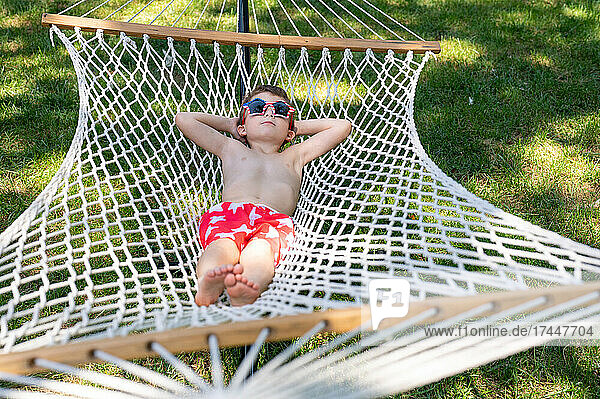 Boy sunning himself on a hammock in swimsuit and silly sunglasses