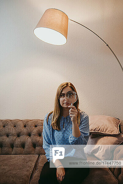 woman holding magnifying glass at home bored
