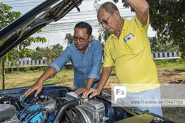 two men looking under the hood of American muscle car in Thailand