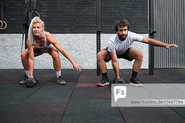 Young man and woman lifting dumbbells at a crossfit gym.