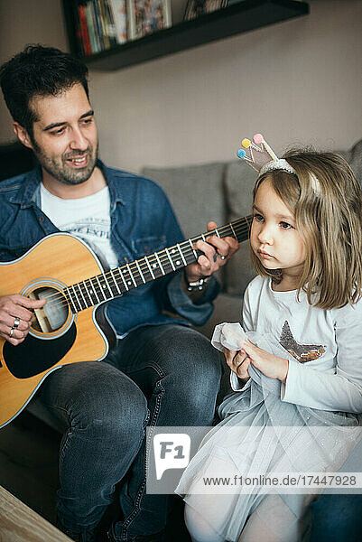 A father playing guitar to his daughter.