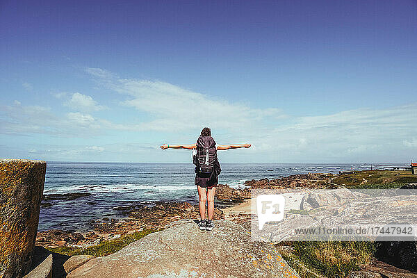 pilgrim woman with open arms on top of a rock looking at the horizon