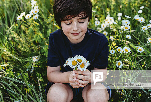 Young boy holding a bouquet of daisies in a field of flowers.