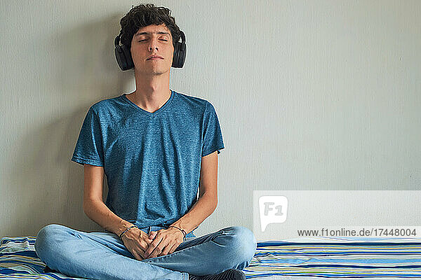 Young man sits in lotus position on the couch  listens to music.