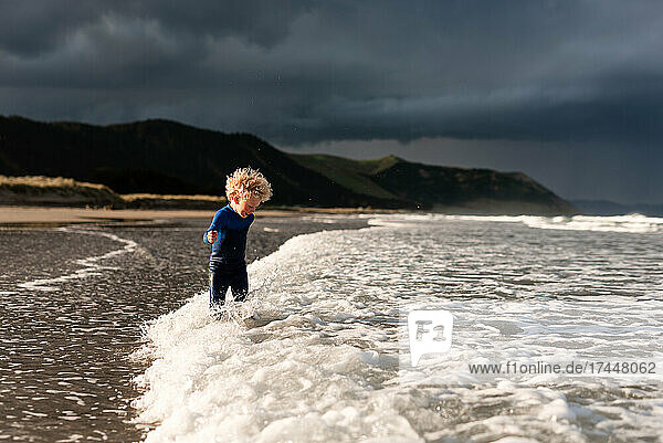 Curly haired kid playing in waves at beach in New Zealand