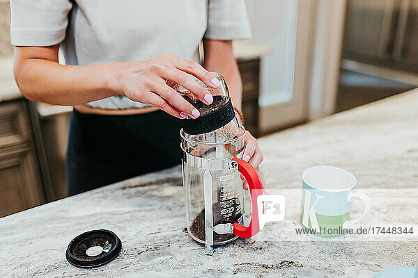 Woman pours freshly ground coffee beans into French press in kitchen