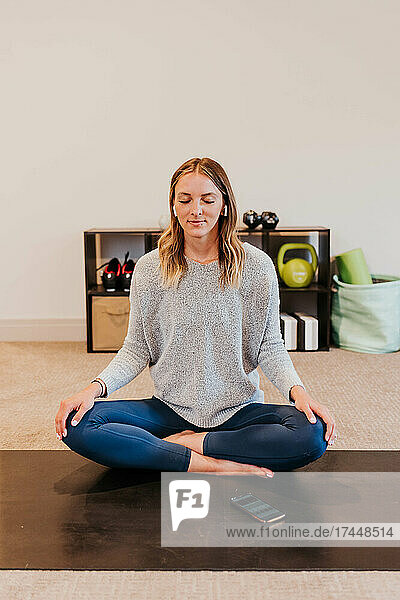 Woman wears earbuds while meditating in home gym