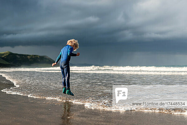 Young boy jumping waves at beach on cloudy day