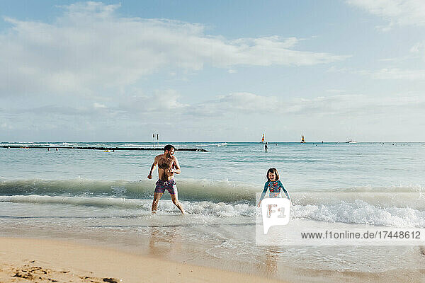 Father and daughter play in ocean on beach in Waikiki