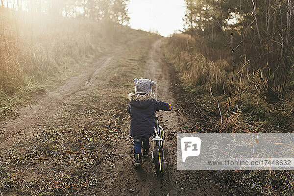 Boy pushing his bike up muddy hill in forest