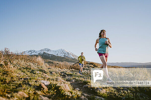 A woman and man trail run in the mountains during golden hour