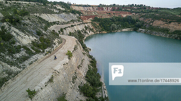 A motorbike driving near a cliff above a lake  Aerial drone shot