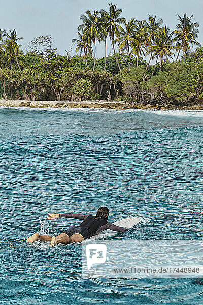 Male surfer in ocean near desert beach Maldives