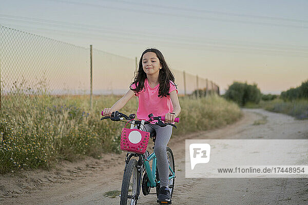 Happy girl riding a bike on a road in the field at sunset