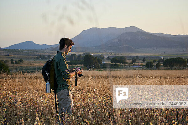 Photographer with a backpack holds a camera in a meadow at sunset