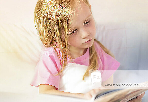 A little girl reads a book before bed in her bed