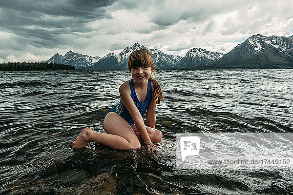 Young girl sitting in mountain lake on a cloudy day