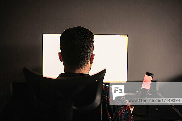 Rear view of man sitting at desk working on computer