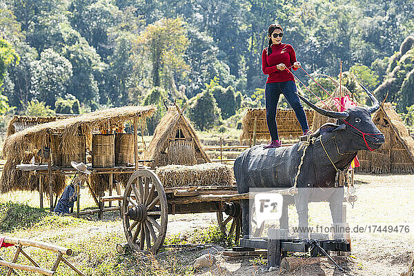 woman posing on bull sculpture at traditional village in Thailand