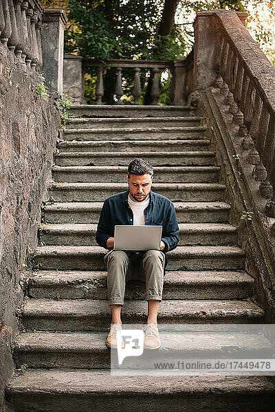 Man using laptop computer sitting on steps in city
