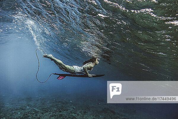 Male surfer holding surfboard while diving undersea at Maldives