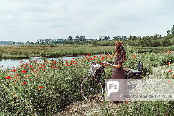 Woman with bicycle standing among poppies field against sky