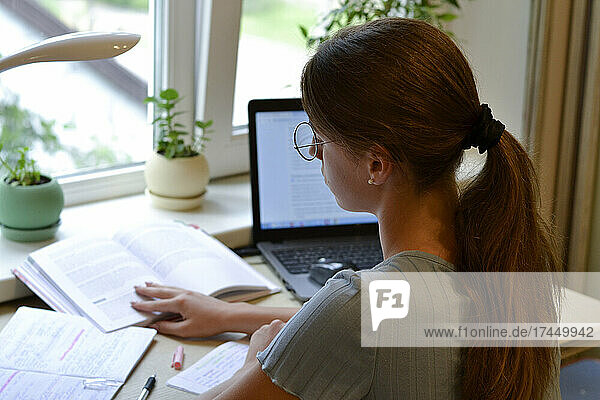 girl student studying at home with books and laptop