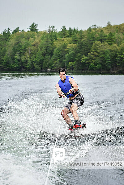 Man wake boarding while being pulled by a boat on a lake.