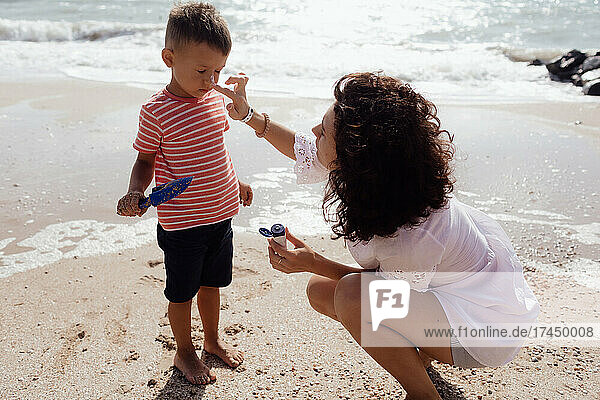 Caring mom smears sun cream on her son on the seashore