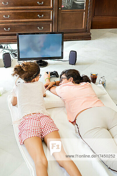 Mother and daughter lying on floor playing video game together at home