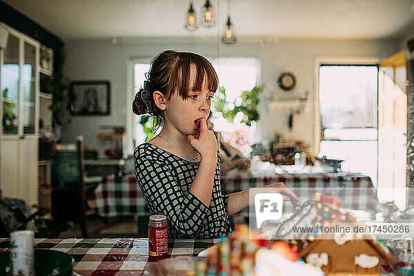 Young girl licking finger while decorating gingerbread house