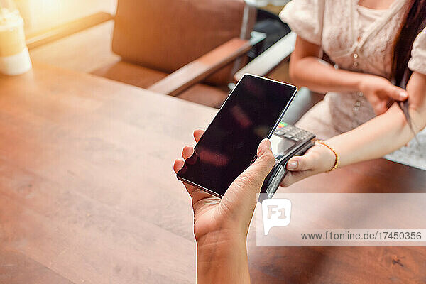 woman holding smartphone close to electronic payment machine