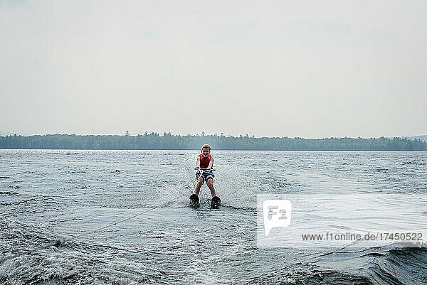 Tween boy waterskiing on lake with trees in background